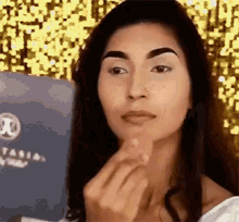 a woman is applying makeup to her face in front of a box of anastasia beverly hills products .