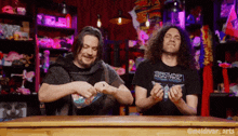 two men sitting at a table with one wearing a ground control shirt