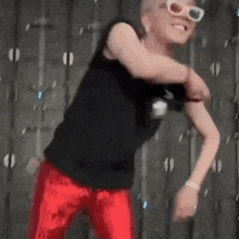 a man wearing a black tank top and red pants is dancing in front of a wall .