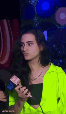 a woman in a neon green jacket is holding a microphone and talking into it