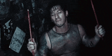 a man in a tank top is holding a pair of drumsticks in his hands .