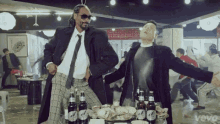 snoop dogg and psy are dancing in a room with bottles of beer .