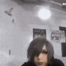 a person with long hair is standing in a room with a fan on the wall .