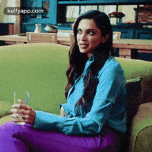 a woman is sitting on a green couch holding a glass of wine .