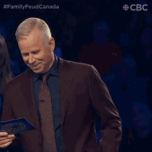 a man in a suit and tie is smiling while holding a clipboard with the word family feud on it