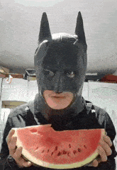 a man in a batman mask holding a slice of watermelon
