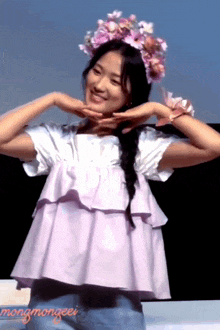 a woman wearing a flower crown makes a heart shape with her hands in front of her face