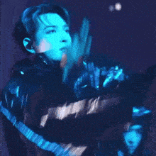 a man in a black jacket is dancing on a stage in front of a blue light .
