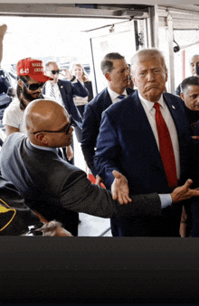 a man wearing a red hat that says make america great again shakes hands with donald trump