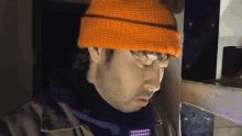 a man wearing an orange beanie is looking down