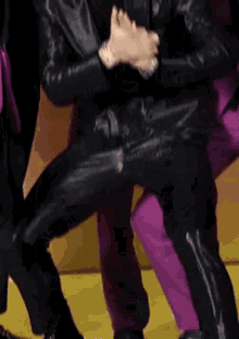 a man in a black leather jacket and pants is dancing on a stage with other people .