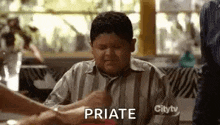 a fat boy is sitting at a table with a bunch of people holding his hands and says `` priate '' .