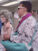 a man wearing sunglasses and a purple shirt is holding a blue bag