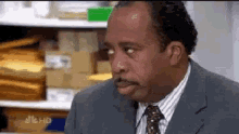 a man in a suit and tie is sitting in front of a shelf .