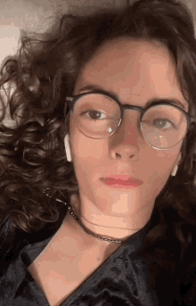 a woman with curly hair wearing glasses and a choker