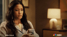 a woman is looking at her phone with a nbc logo in the corner