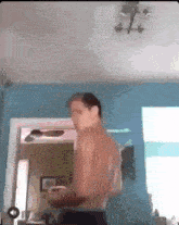 a shirtless man is standing in a room with a ceiling fan and a mirror .