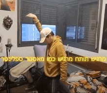 a man wearing a yellow hoodie and a white hat is dancing in a room with hebrew writing on the wall