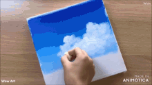 a person is painting a picture of clouds on a canvas