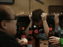 a group of people are sitting at a table with bottles of beer and a sign that says " you bastards "
