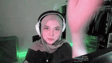 a woman wearing a hijab and headphones is sitting at a desk .