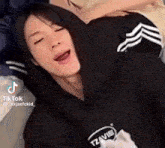 a person wearing a black hoodie is laying down with their eyes closed and their mouth open .