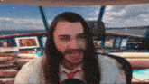 a man with long hair and a beard is sitting in front of a microphone in a video call .