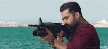 a man holding a gun in front of a body of water with nandamurifans.com written on the bottom