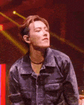 a young man is standing on a stage wearing a denim jacket and a pearl necklace .