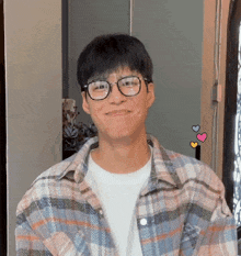 a young man wearing glasses and a plaid shirt smiles for the camera .