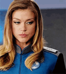 a woman with long blonde hair is wearing a blue jacket with a patch on it that says ' a ' on it .