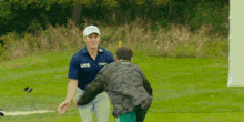 a man wearing a blue shirt with the word uno on it talks to another man on a golf course .