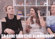 three women are sitting on a couch laughing and one is holding a phone .