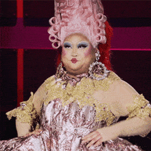a drag queen is wearing a pink wig and a gold dress