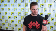 a man is holding a microphone in front of a wall that says comic con on it
