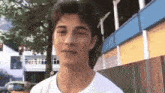a young man in a white t-shirt is standing in front of a building with his eyes closed .