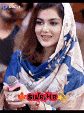 a woman with a scarf around her head is holding a microphone and the word sulei me is on the bottom right