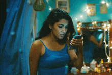 a woman in a blue tank top is looking at her phone in front of a mirror