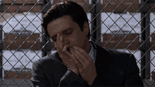 a man in a suit is sitting in front of a chain link fence covering his face with his hands .