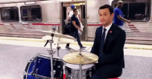a man in a suit and tie is playing a drum set