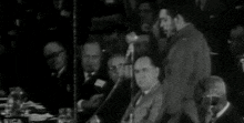 a black and white photo of a man speaking into a microphone in front of a crowd
