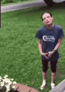 a man in a blue shirt is standing in the grass in front of a flower pot .