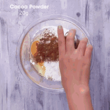 a person is mixing cocoa powder and other ingredients in a glass bowl .