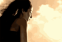 a woman in a black dress is standing in front of a cloudy sky .