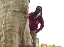 a man wearing a red sweater with a crest on it stands next to a tree