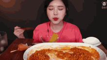 a woman in a pink shirt is eating a plate of food