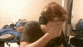 a man wearing headphones covering his face in a messy room