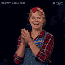 a woman in overalls and a plaid shirt is clapping her hands and smiling .