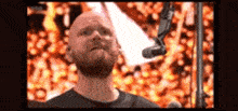 a bald man with a beard is singing into a microphone .