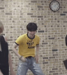 a man in a yellow shirt is dancing in front of a brick wall and a clock .
